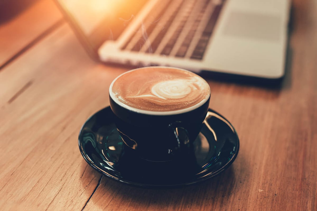 Tasse mit Kaffee neben einem Laptop auf einem Holztisch.