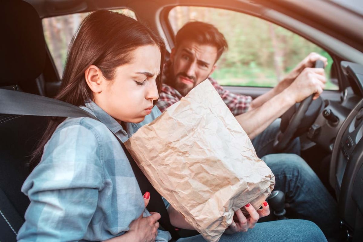 Frau leidet unter Reiseübelkeit und übergibt sich im Auto in eine Tüte.