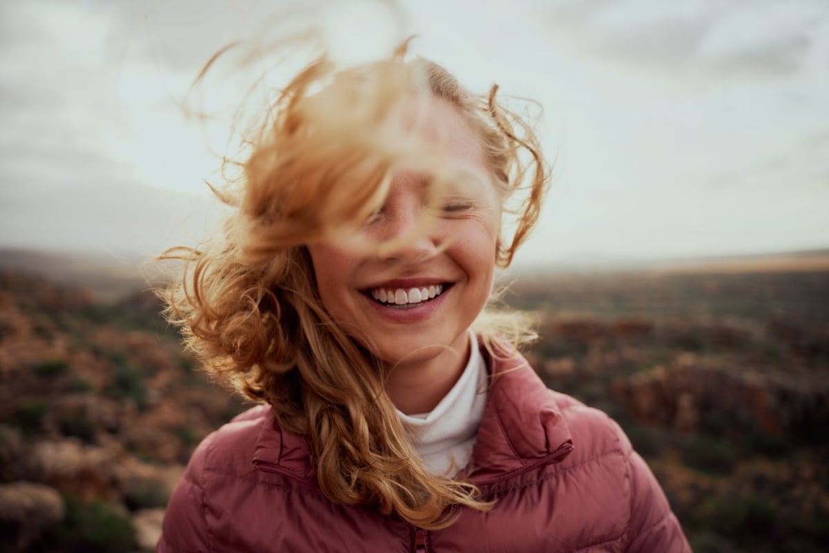 Eine lachende Frau mit rotblonden, wehenden Haaren und geschlossenen Augen.
