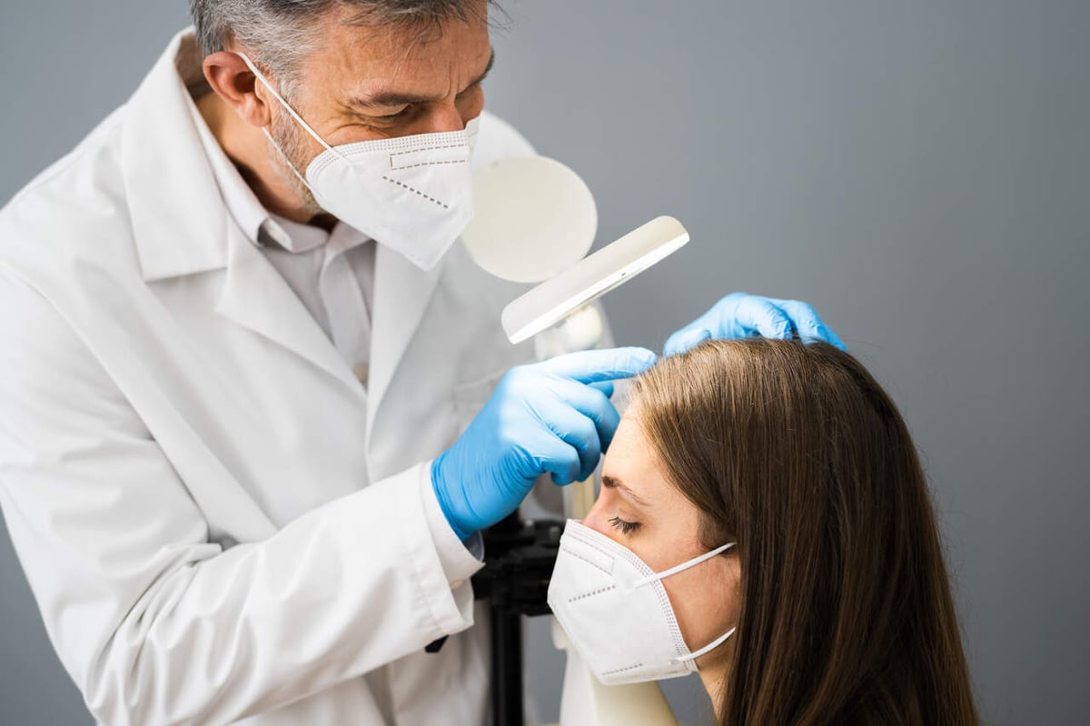 EIn Dermatologe untersucht die Kopfhaut einer jungen Frau.