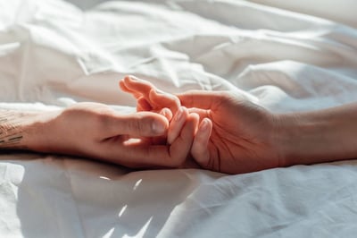 Auf einem Bettlaken berühren sich die Hände von Mann und Frau.