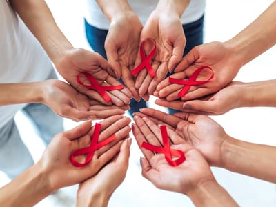 Zum Welt AIDS Tag: Solidarität mit den Betroffenen. Viele Hände halten rote Schleifen.