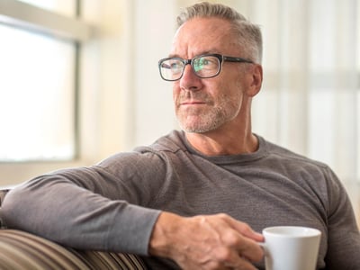 Ein Mann mittleren Alters sitzt mit einer Kaffeetasse auf dem Sofa.