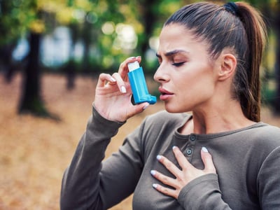 Eine junge Frau steht im Wald und benutzt Asthmaspray.