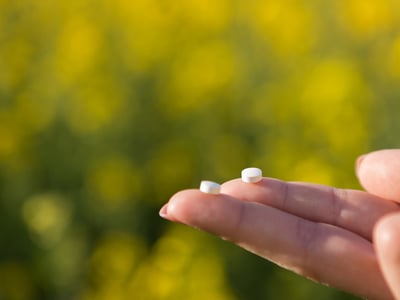 Zwei kleine weiße Tabletten werden auf den Fingerspitzen gehalten.