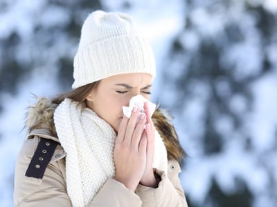 Eine Frau mit winterlicher Kleidung und Schnee im Hintergrund putzt sich die Nase.