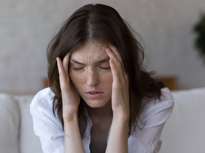 Junge Frau mit Sommersprossen hat Kopfschmerzen und hält sich den Kopf.