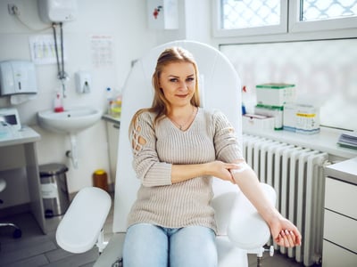 Eine junge Frau hat soeben Blut gespendet. Sie hat ein Pflaster auf dem Arm und übt mit einer Hand Druck auf die Einstichstelle aus.