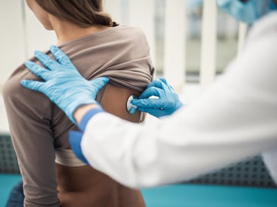 Ein Arzt hört mit dem Stethoskop am Rücken einer Patientin die Lunge ab.