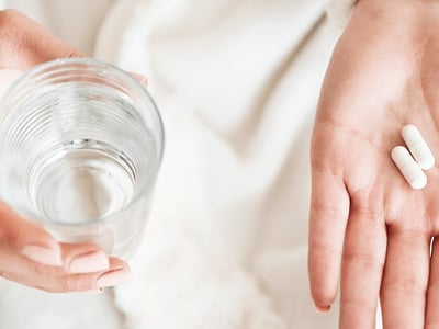 Antibiotika Tabletten in Hand und ein Glas Wasser dazu.