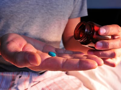 Aus einer Glasflasche schüttet ein Mann sich eine blaue Tablette auf die Handfläche.