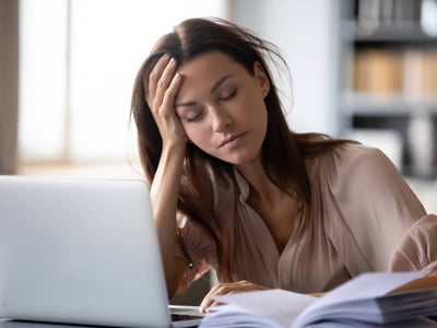 Müde Frau mit aufgestütztem Kopf vor dem Laptop.