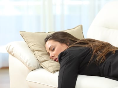 Eine junge Frau ist sehr müde und schläft auf dem Sofa.