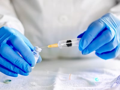 Hände mit blauen Handschuhen bereiten eine Spritze mit Impfstoff vor.