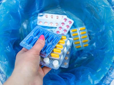 Eine Frauenhand wirft mehrere Tabletten in einen Mülleimer.