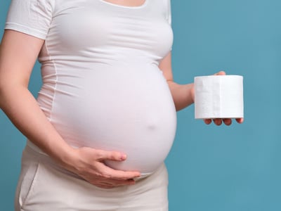 Hämorrhoiden in der Schwangerschaft: Hochschwangere Frau hält eine Rolle Klopapier neben ihrem Bauch.