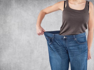Frau hält zu große Jeanshose mit einer Hand an der Hüfte.