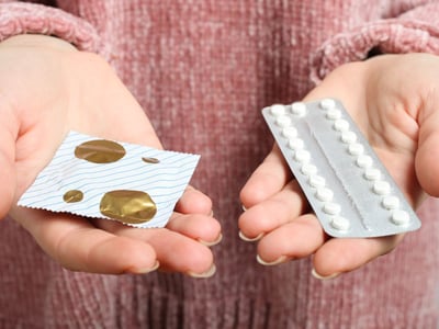 Welche Verhütungsmittel und Verhütungsmethoden gibt es? Eine Frau hält die Antibabypille und ein Kondom in ihren Händen.