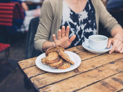 Eine Frau trinkt Kaffee und lehnt das angebotene Brot ab.