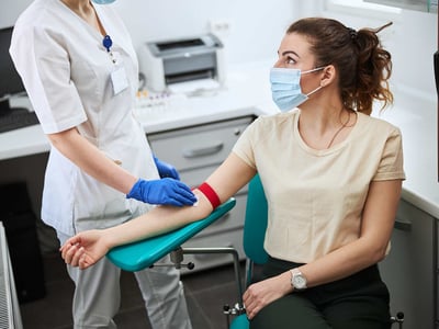 EIne Arzthelferin nimmt bei einer Frau Blut ab.