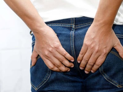 Person in Jeans hält sich den Po mit beiden Händen.