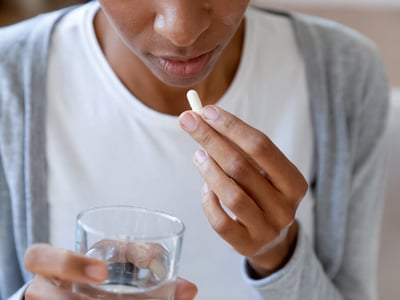 Eine Frau nimmt Antibiotika als Kapseln mit einem Glas Wasser ein.