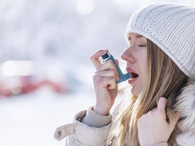Junge Frau benutzt im Winter einen Asthma-Inhalator.