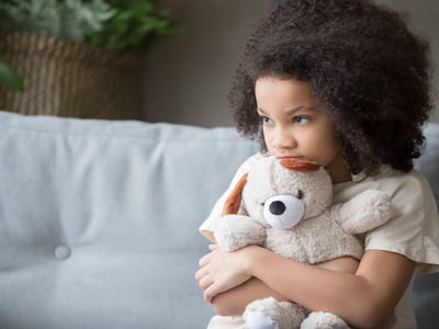 Trauriges Mädchen mit Teddybär auf Sofa.