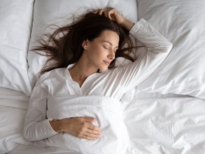 Eine Frau schläft in einem Bett mit weißen Bettbezügen.