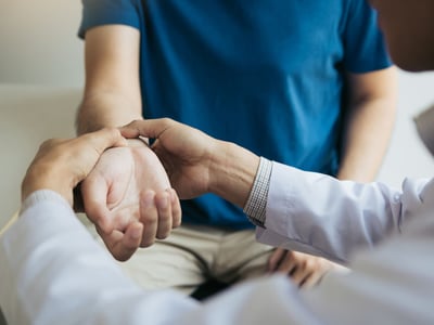 Arzt untersucht Handgelenk von Patientin.