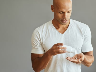 Ein junger mann mit Glatze schüttet sich Tabletten in die Hand.