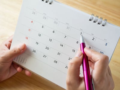 Auf einem Kalender werden mit einem Stift Daten eingetragen.