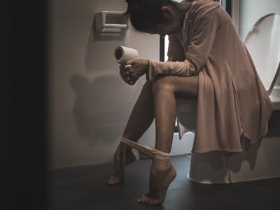 Eine Frau sitzt im Dunkeln mit Schmerzen auf der Toilette.
