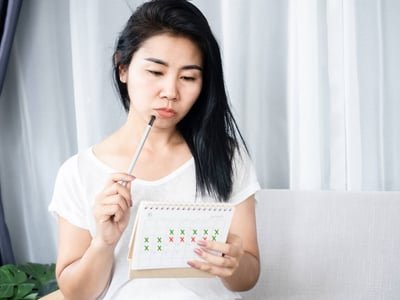 Frau betrachtet mit Stift am Mund ihren Kalender.