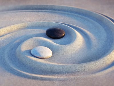 Ying und Yang wurde in den Sand gezeichnet. Die Symbolik wird durch einen schwarzen und einen weißen Stein verdeutlicht.