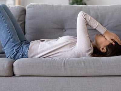 Eine Frau hat vestibuläre Migräne und liegt mit Kopfschmerzen und Schwindel auf dem Sofa.