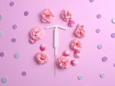 Bunte Darstellung einer Hormonspirale mit pinkem Hintergrund und Blumen.