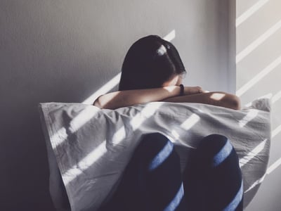 Junge Frau mit Migräne sitzt mit Kopfschmerzen und Übelkeit in einem abgedunkelten Raum.