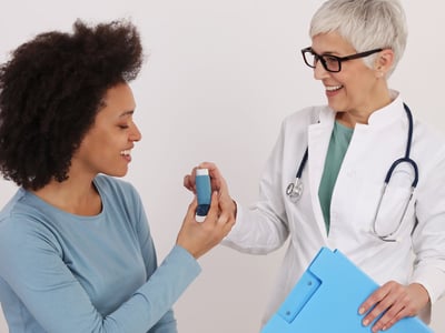 Eine Ärztin reicht einer Patientin mit Asthma einen Inhalator.