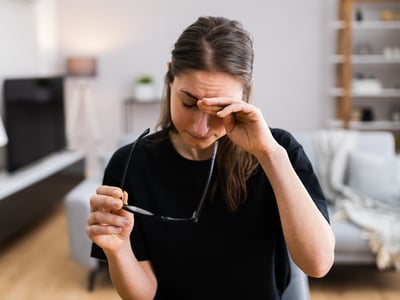 Frau am Schreibtisch hält eine Brille in der Hand und reibt sich die Augen.