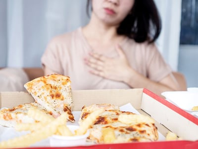 Frau hält sich die Hand an das Brustbein, nachdem sie Pizza und Pommes gegessen hat.
