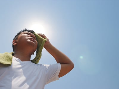 Mann trocknet schwitzendes Gesicht mit grünem Handtuch in der prallen Sonne