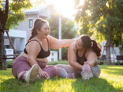 Zwei Übergewichtige Frauen machen Yoga-Übungen im Park und haben Spaß dabei.