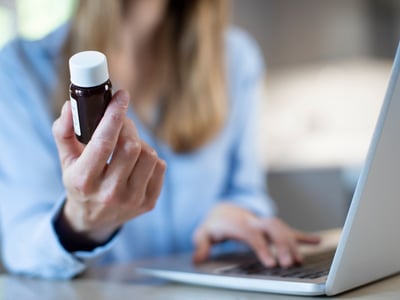 Frau sitzt am Laptop und bestellt Medikamente nach.
