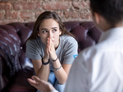 Mädchen sitzt auf einer Ledercouch, sie guckt besorgt. Vor ihr sitzt eine Psychotherapeutin.