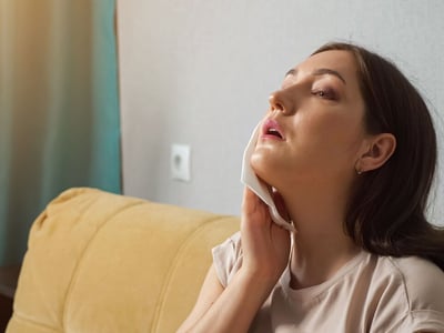 Frau hält kühlenden Lappen in schwitzendes Gesicht.