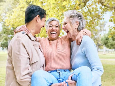 Drei ältere Frauen lachen im Park.