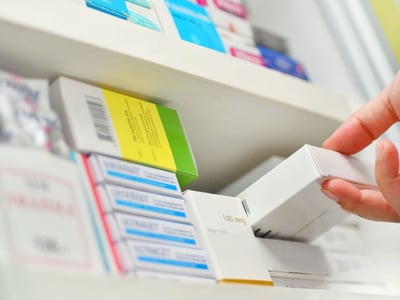 Apotheker oder Apothekerin nimmt Tabletten in Schachtel aus einem Regal.