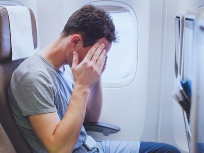 Mann sitzt im Flugzeug und hält sich die Hände vor das Gesicht.
