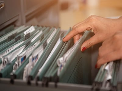 Frauenhände blättern durch Patientenakten in einem Hängeregister.